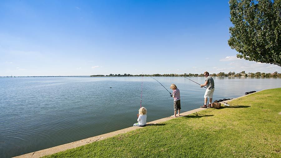 A man and two young children fishing on the banks of Lake Mulwala